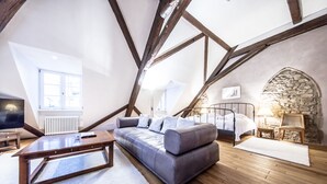 Un dormitorio tipo loft con vigas de madera a la vista, un sofá gris, una cama con dosel blanco, una pared de piedra y vistas al exterior.