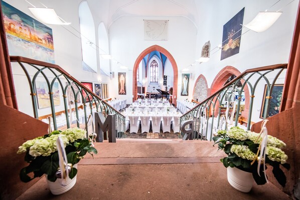 A grand staircase leading to a banquet hall with white tables and chairs, flanked by potted plants and framed artwork. - Ulner Kapelle (Weinheim)