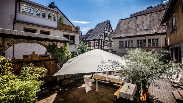 Un patio con una mesa y sillas bajo una carpa, rodeado de edificios tradicionales.