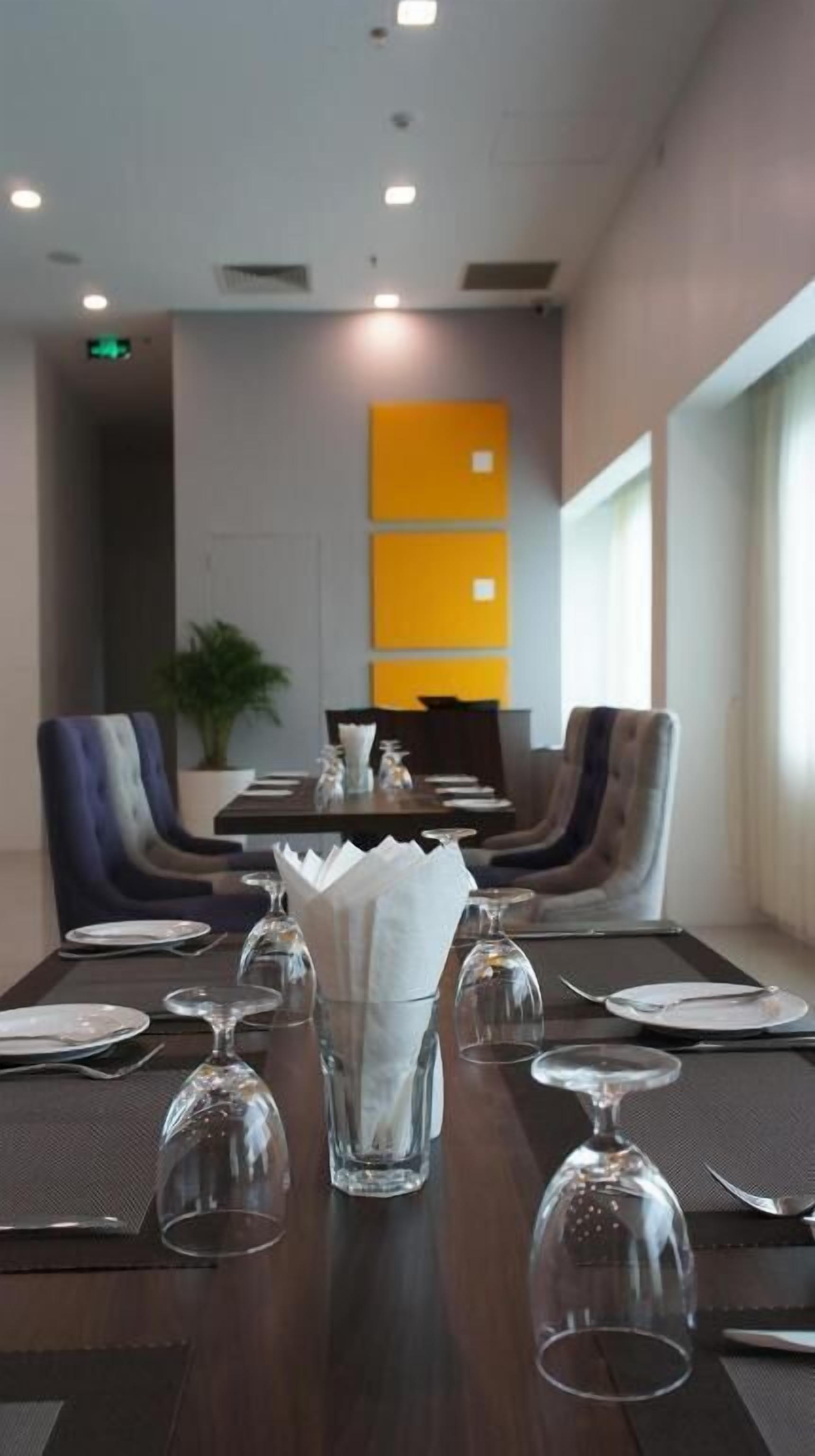 Un salón de conferencias con una larga mesa dispuesta para una reunión, equipado con sillas, una planta y una moderna pared de acento amarilla.