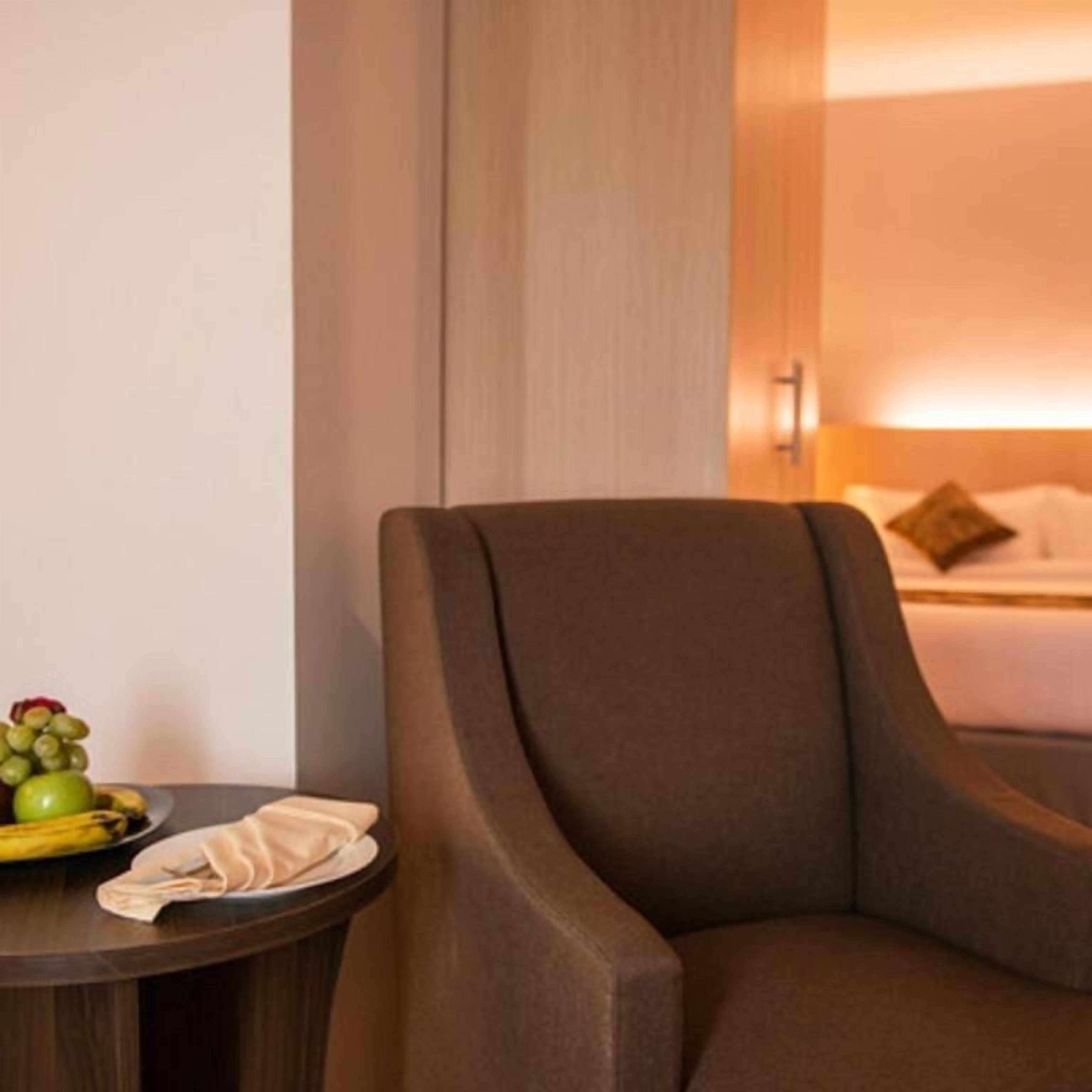 Habitación de hotel con un sillón marrón, una mesita redonda con fruteros, un plato y una servilleta.