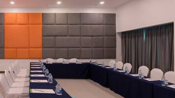 Un salón de conferencias con una larga mesa, sillas blancas y una pared acolchada.