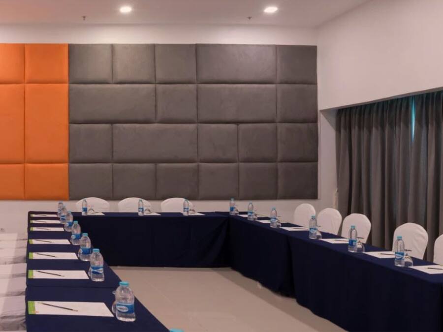 Uma sala de conferências com uma mesa comprida, cadeiras brancas e uma parede acolchoada.