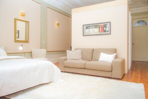 A bedroom with a bed, a sofa, a white rug, a framed picture on the wall, and a door in the background. - Liiiving in Porto - Art & Heart Studio (Porto)