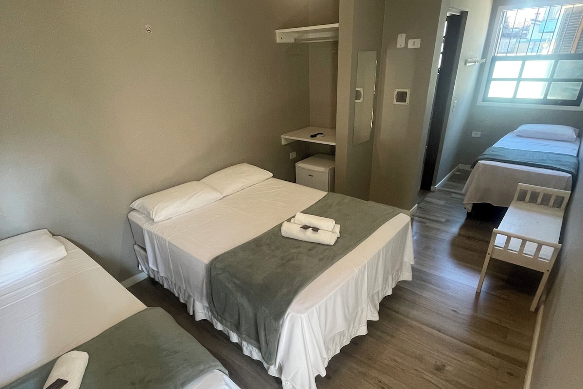A hotel room with two single beds, a small desk, a chair, a mirror, and a ceiling fan.