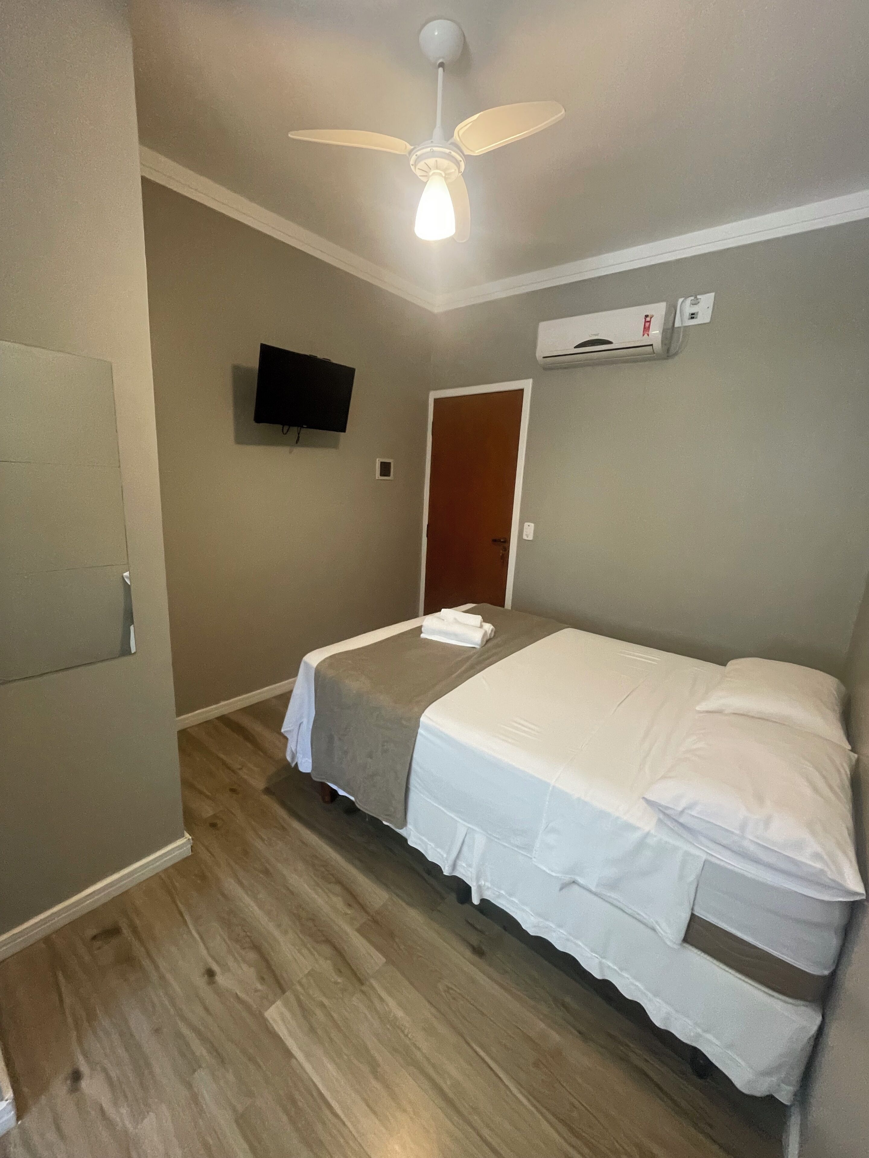 Hotellihuone, jossa on sänky, kattotuuletin, televisio ja ilmastointilaite.