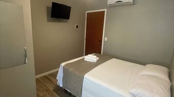 Hotellihuone, jossa on sänky, kattotuuletin, televisio ja ilmastointilaite.