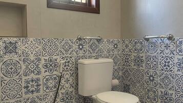 Un baño con inodoro, ventana y baldosas estampadas.