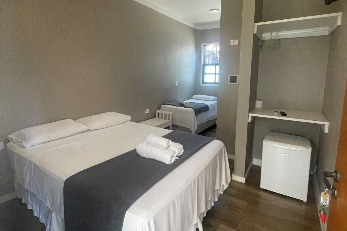 A hotel room with two beds, a ceiling fan, a small refrigerator, and a TV mounted on the wall.