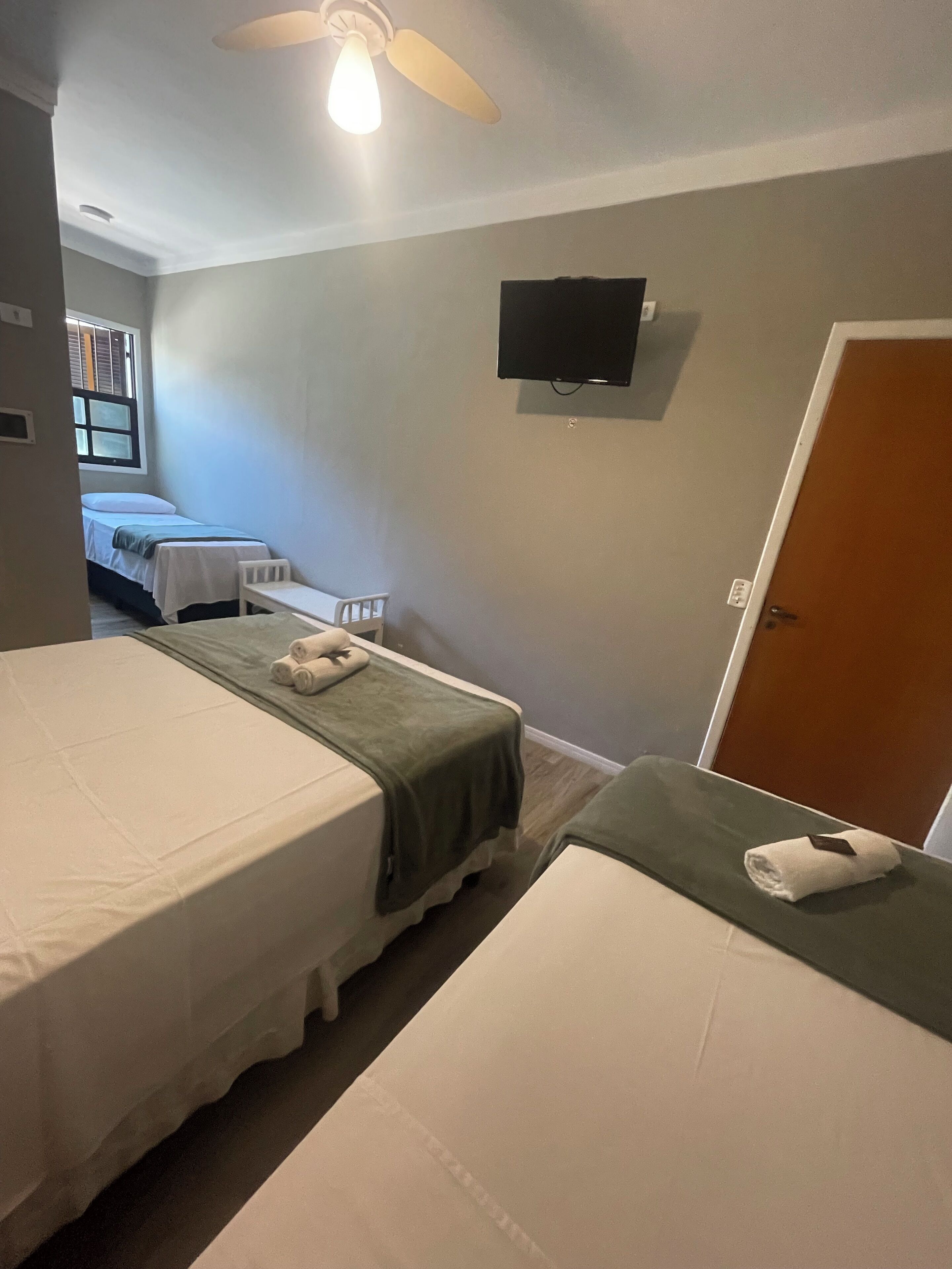 A hotel room with two beds, a TV on the wall, a ceiling fan, and a door.