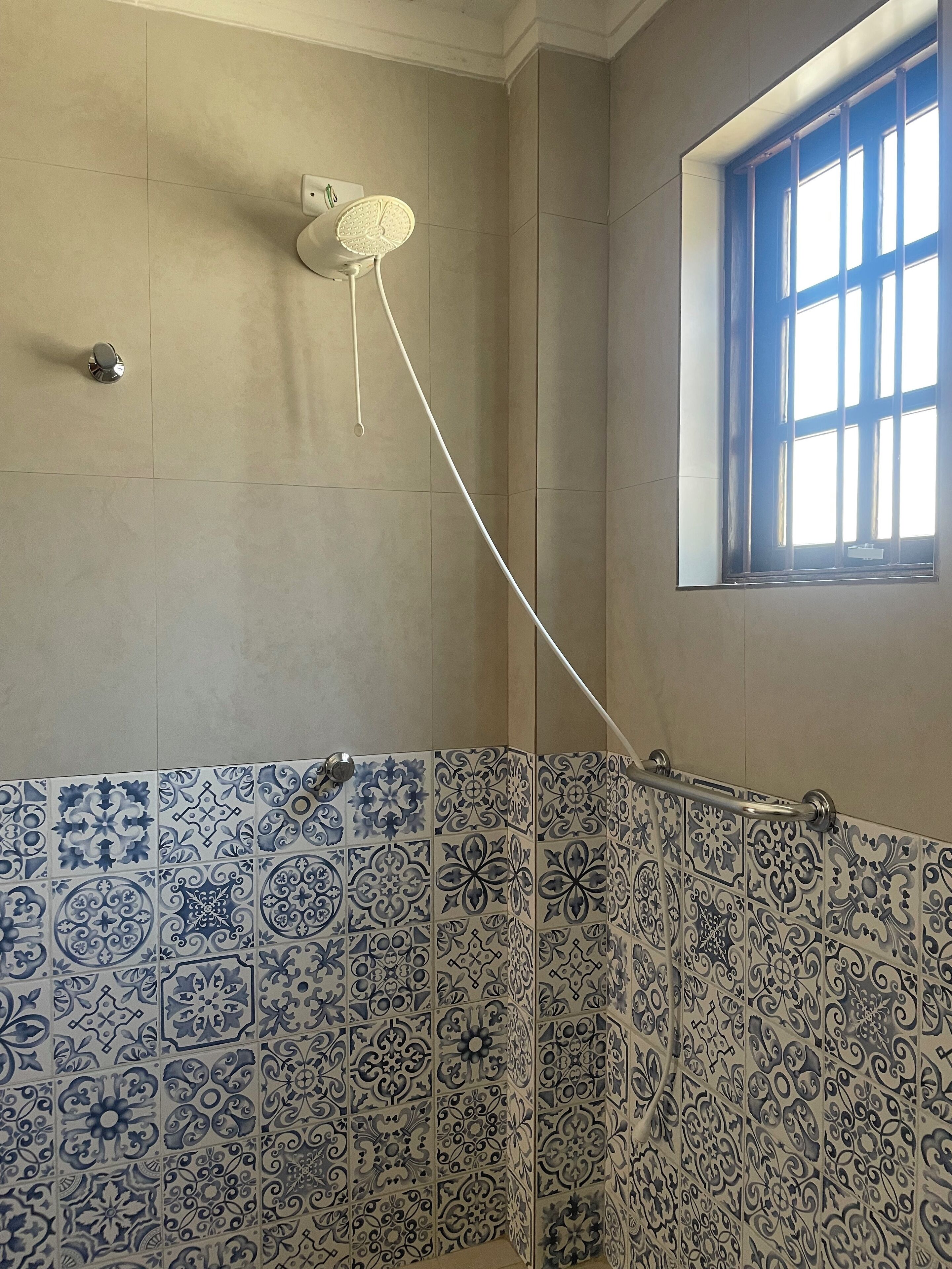 Un baño con ducha, ventana y azulejos decorativos en azul y blanco.