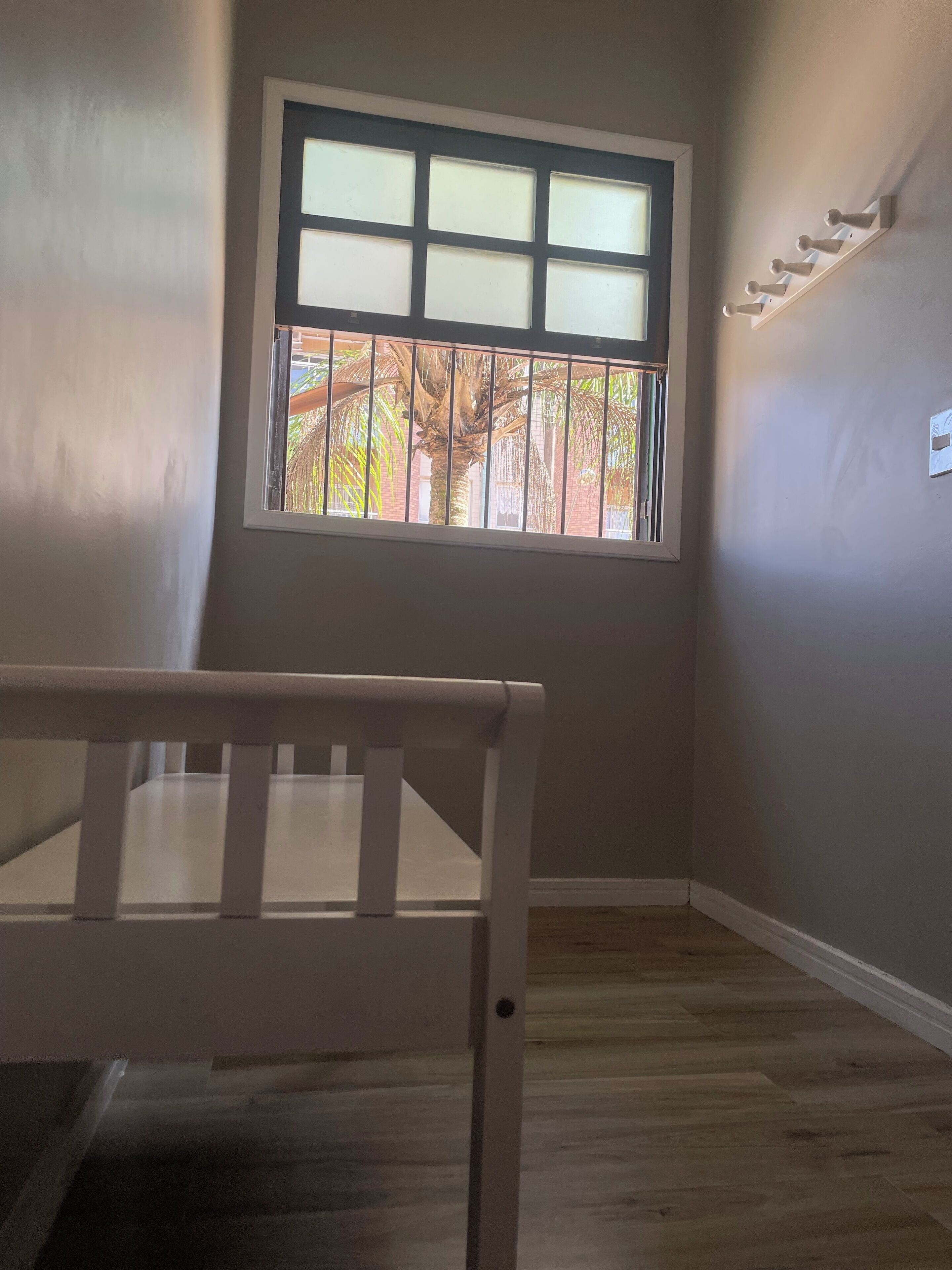 A room with a window, a crib, and a wall-mounted light fixture.
