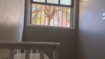 A room with a window, a crib, and a wall-mounted light fixture.
