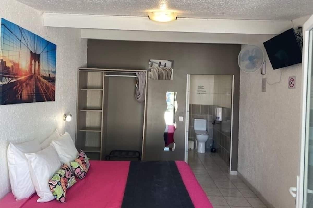 Ein Schlafzimmer mit Bett, einem Bild, einem Kleiderschrank und einem durch eine geöffnete Tür einsehbaren Badezimmer.