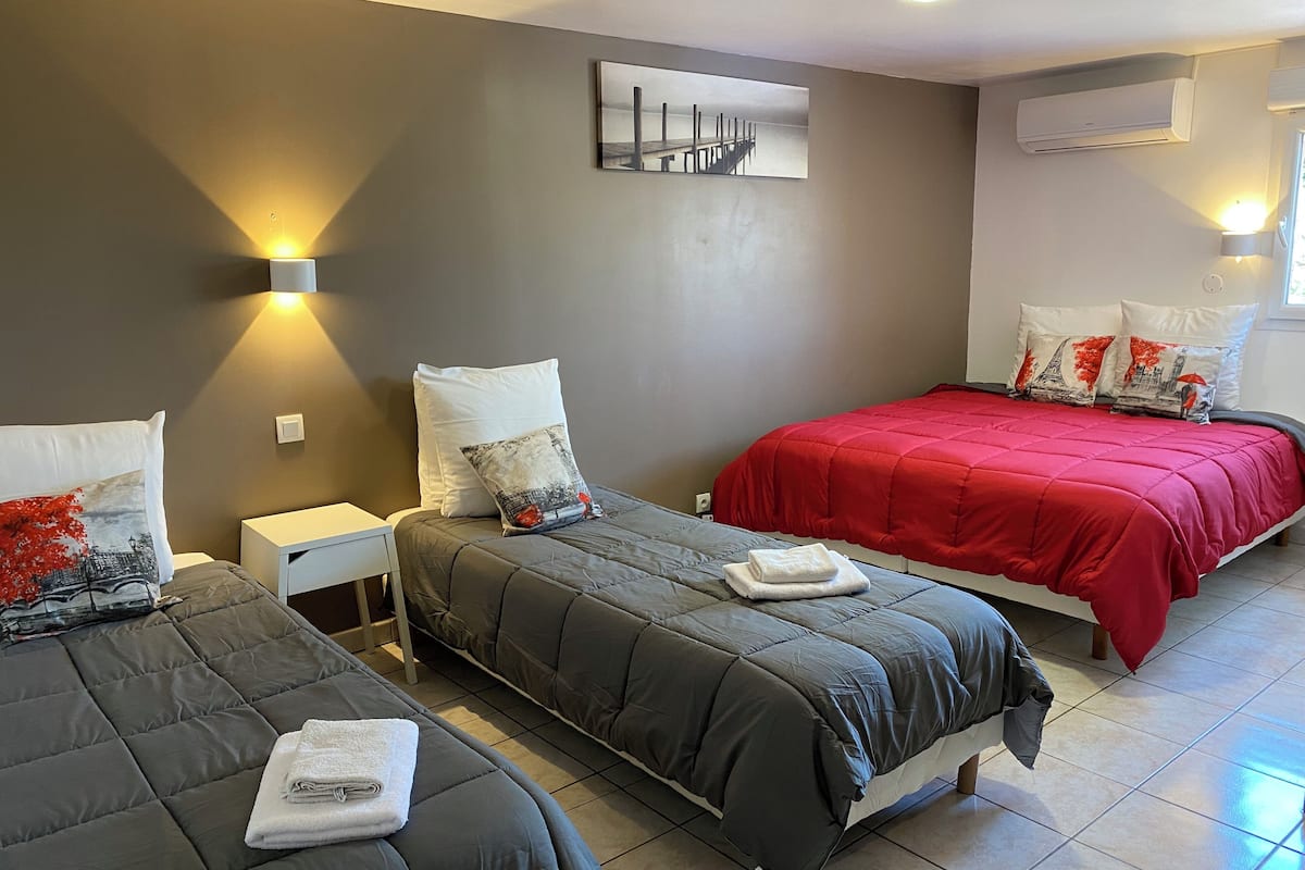Ein Hotelzimmer mit zwei Betten, grauer Bettwäsche, einer roten Tagesdecke und einem Bild an der Wand.