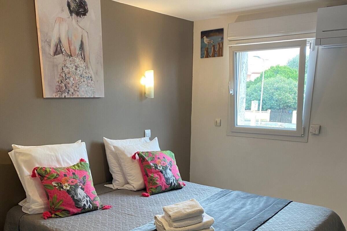 Ein ordentlich gemachtes Bett mit einer grauen Tagesdecke und zwei Kissen, eines davon mit einem Blumenmuster.