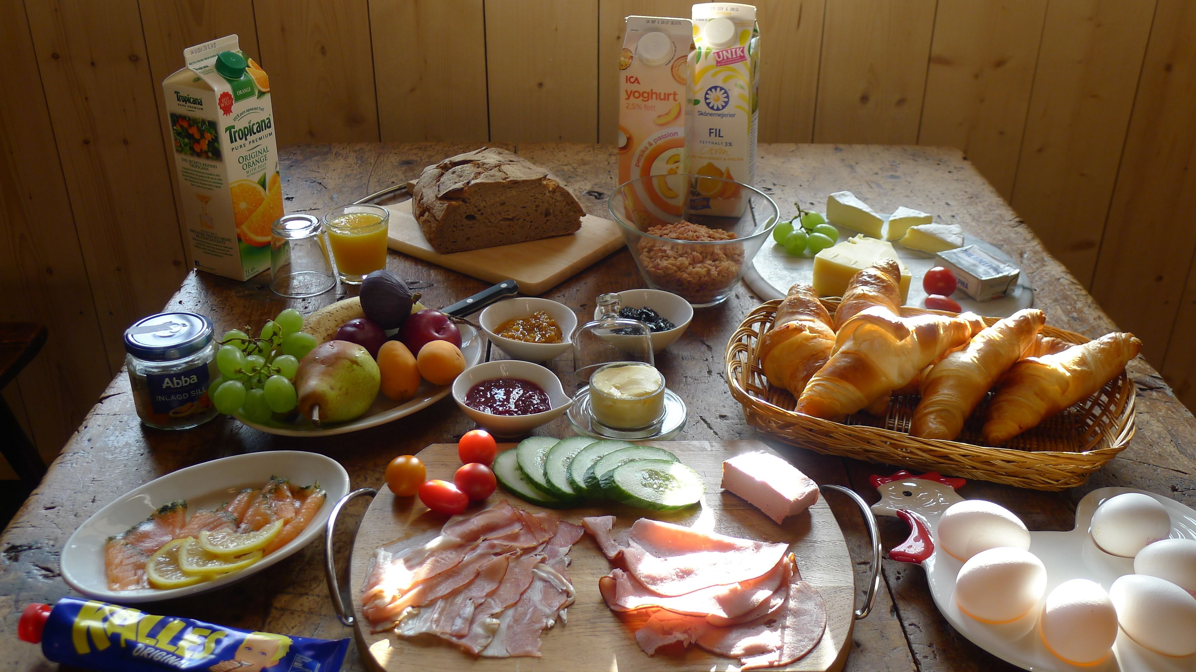 A breakfast table with various food items including bread, cheese, eggs, ham, and fruits.