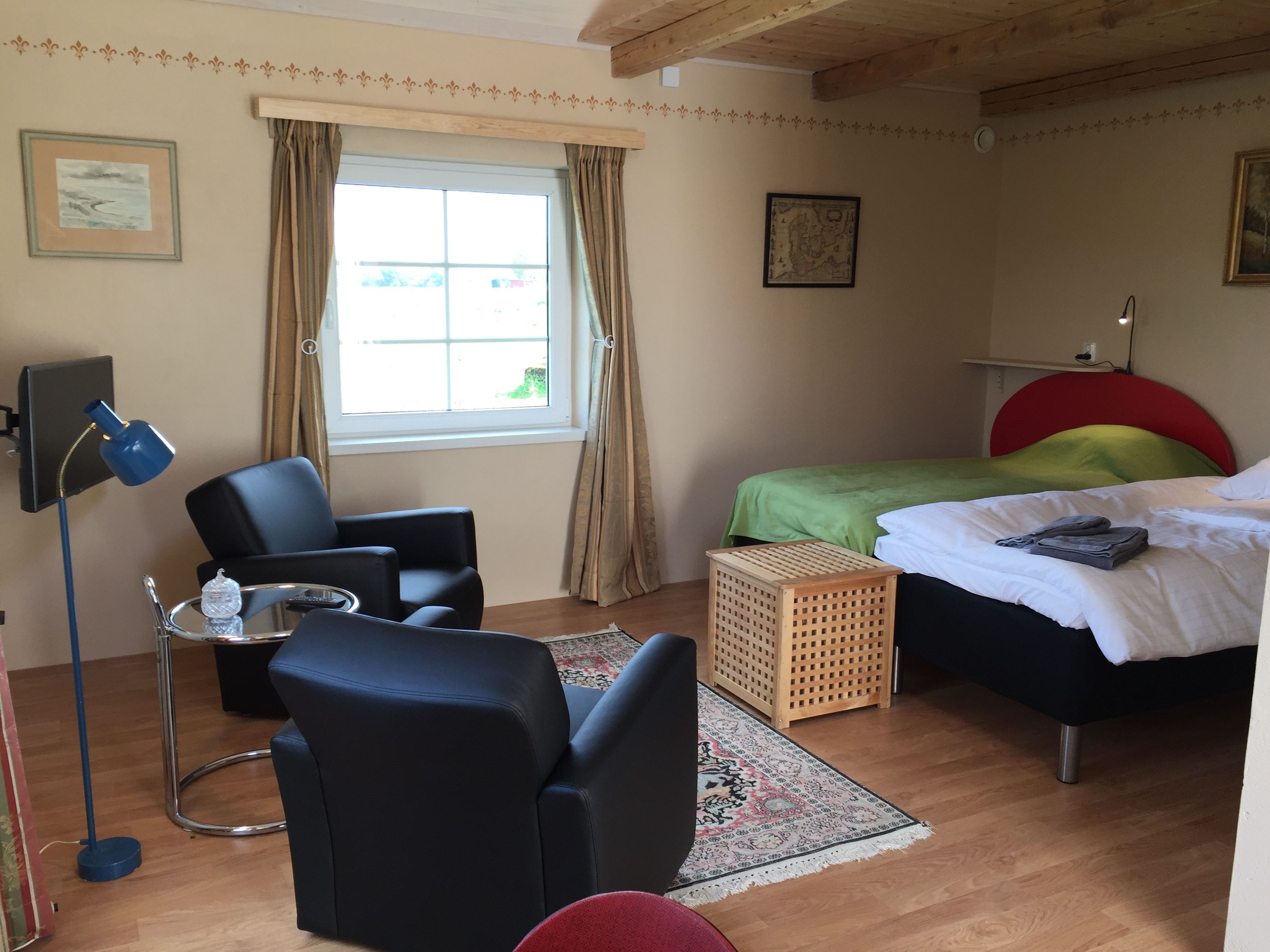 A bedroom with a bed, a desk with a chair, a lamp, and a window with curtains.