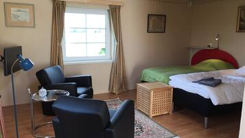 A bedroom with a bed, a desk with a chair, a lamp, and a window with curtains.