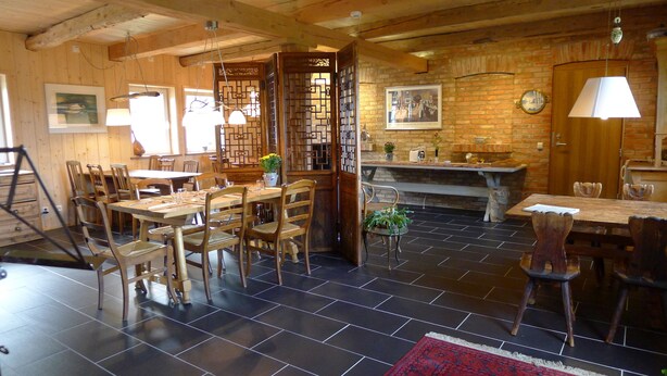 A rustic dining area with wooden tables and chairs, a black-tiled floor, and a brick fireplace. - Lilla Trulla Gårdshotell - Feels like home (Klippan)