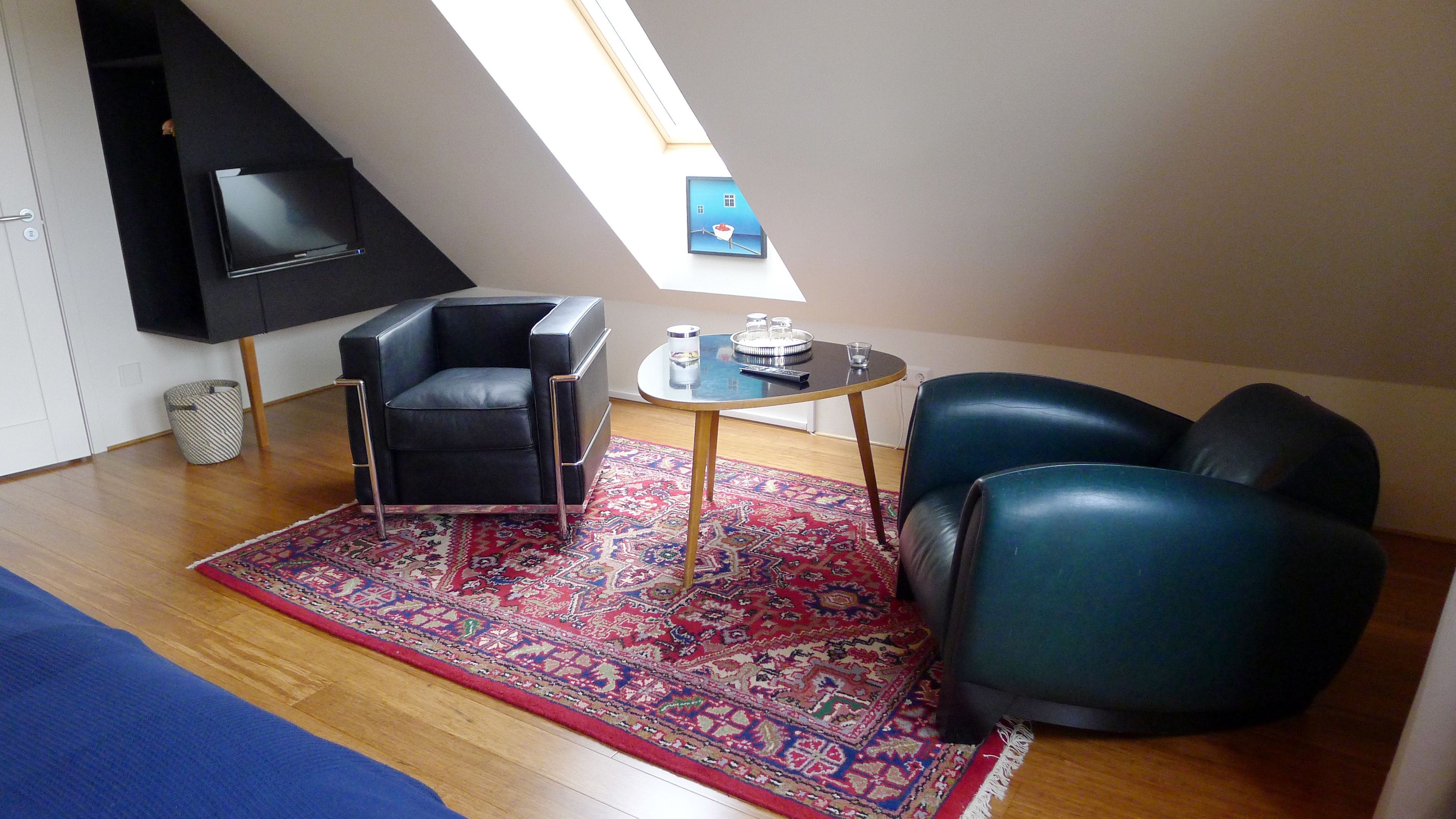 Ein modernes Wohnzimmer mit einem schwarzen Ledersofa, einem schwarzen Ledersessel, einem kleinen runden Tisch und einem farbenfrohen Teppich.