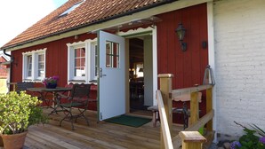 A red wooden house with a wooden deck, a dining area with chairs and a table, and a door leading inside. - Lilla Trulla Gårdshotell - Feels like home (Klippan)