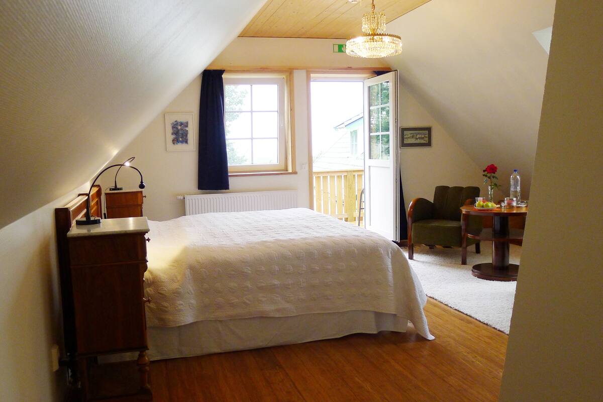 Ein Schlafzimmer mit Bett, Kommode, Schreibtisch mit Stuhl, Fenster und einer Chandelier.