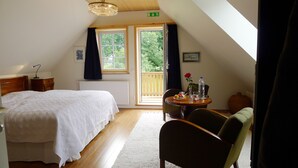 A bedroom with a large bed, a wooden headboard, a nightstand, a desk with a chair, a window with curtains, and a view of the outdoors. - Lilla Trulla Gårdshotell - Feels like home (Klippan)
