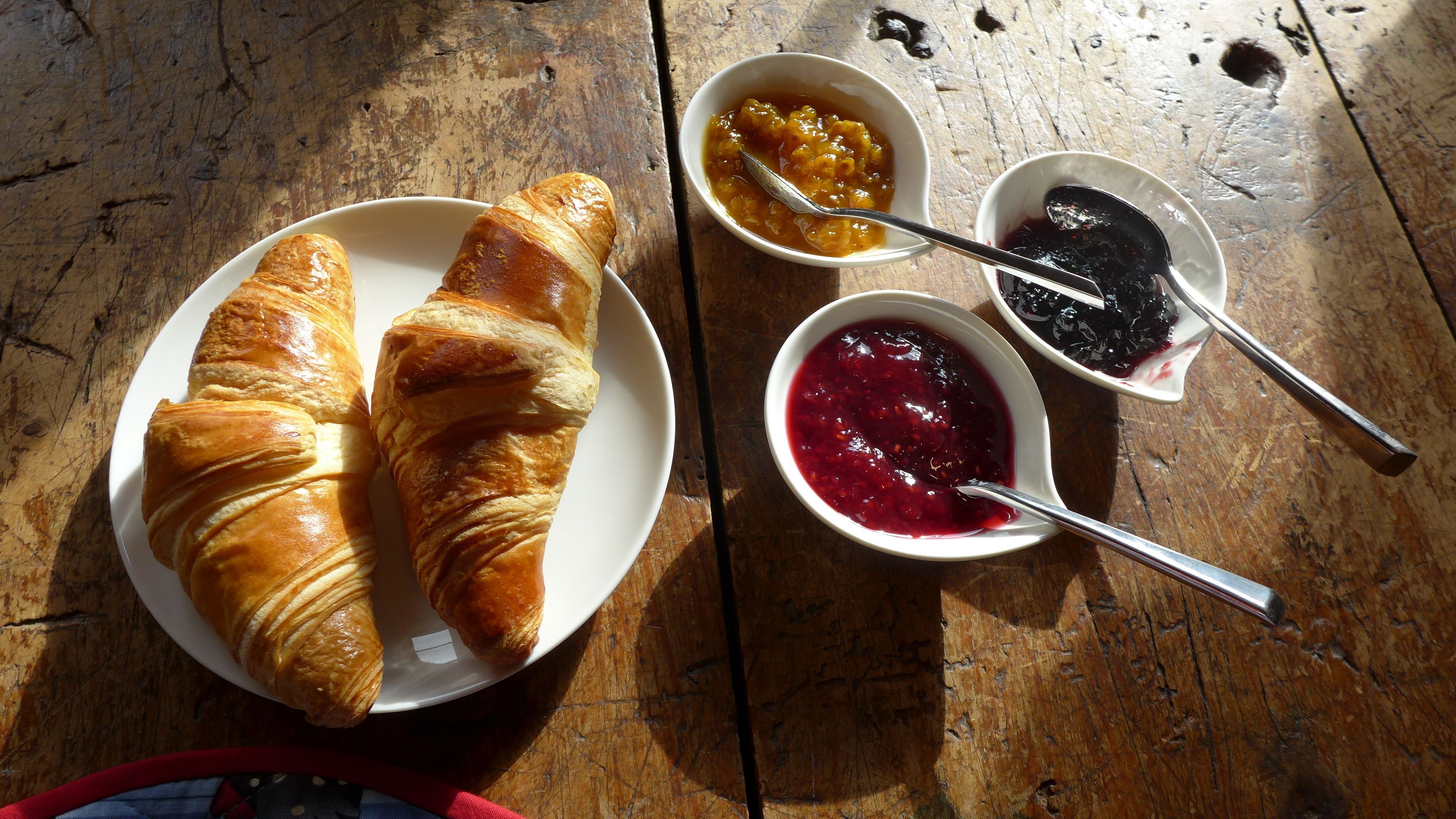 A wooden table with two plates of croissants and two small bowls of jam.