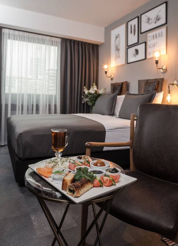 Une chambre d’hôtel avec un lit, une table à manger avec de la nourriture, une chaise et des œuvres d’art accrochées au mur.