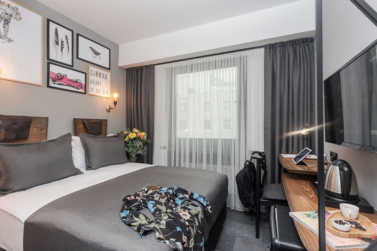 A hotel room with a bed, a desk, a chair, a TV, and a window with curtains.