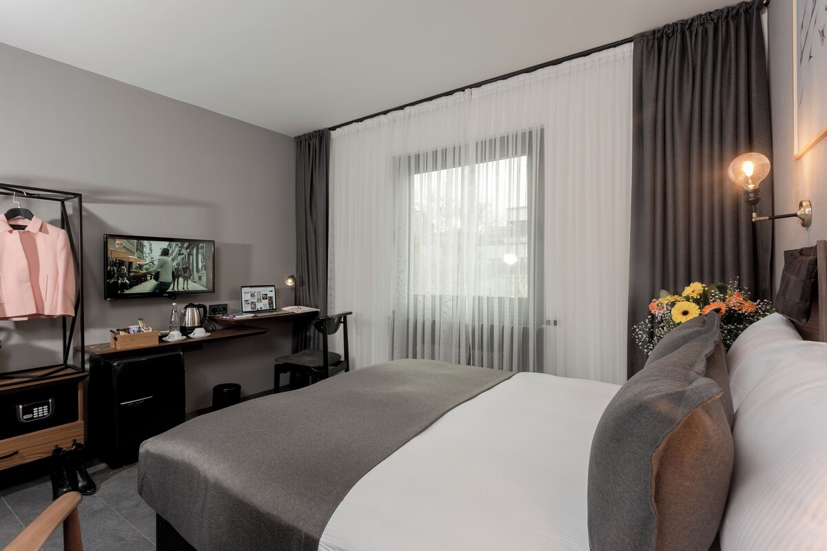 A modern hotel room with a bed, a desk, a TV, and a wardrobe.
