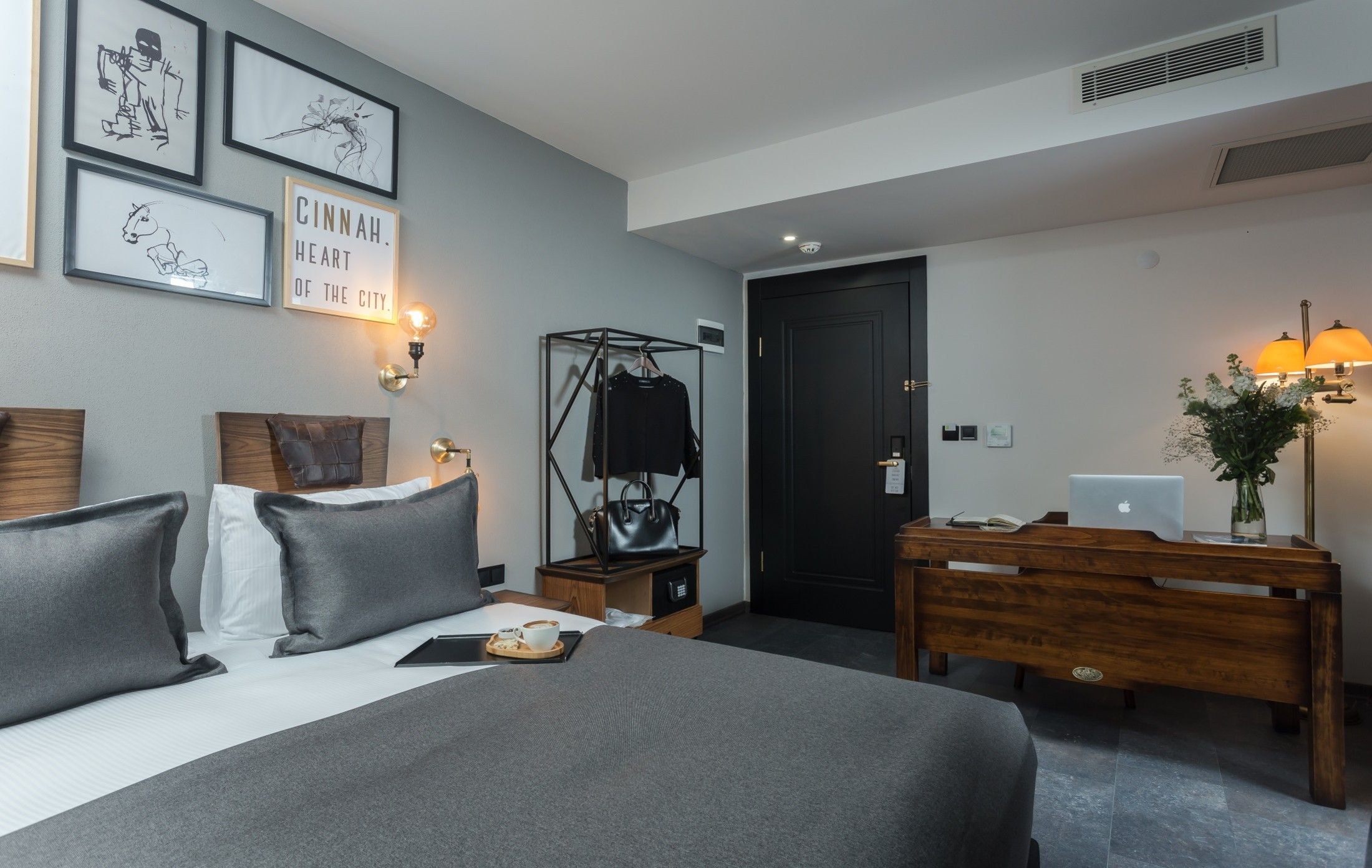 A hotel room with a bed, bedside table, lamp, and a desk with a laptop.