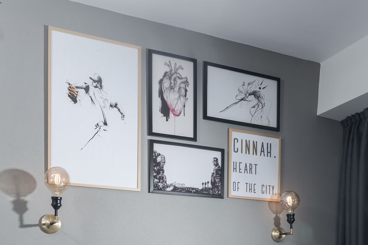 Una pared con cuatro obras de arte enmarcadas, un cartel, dos luces de pared y una cortina.