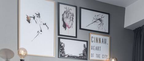 Una pared con cuatro obras de arte enmarcadas, un cartel, dos luces de pared y una cortina.