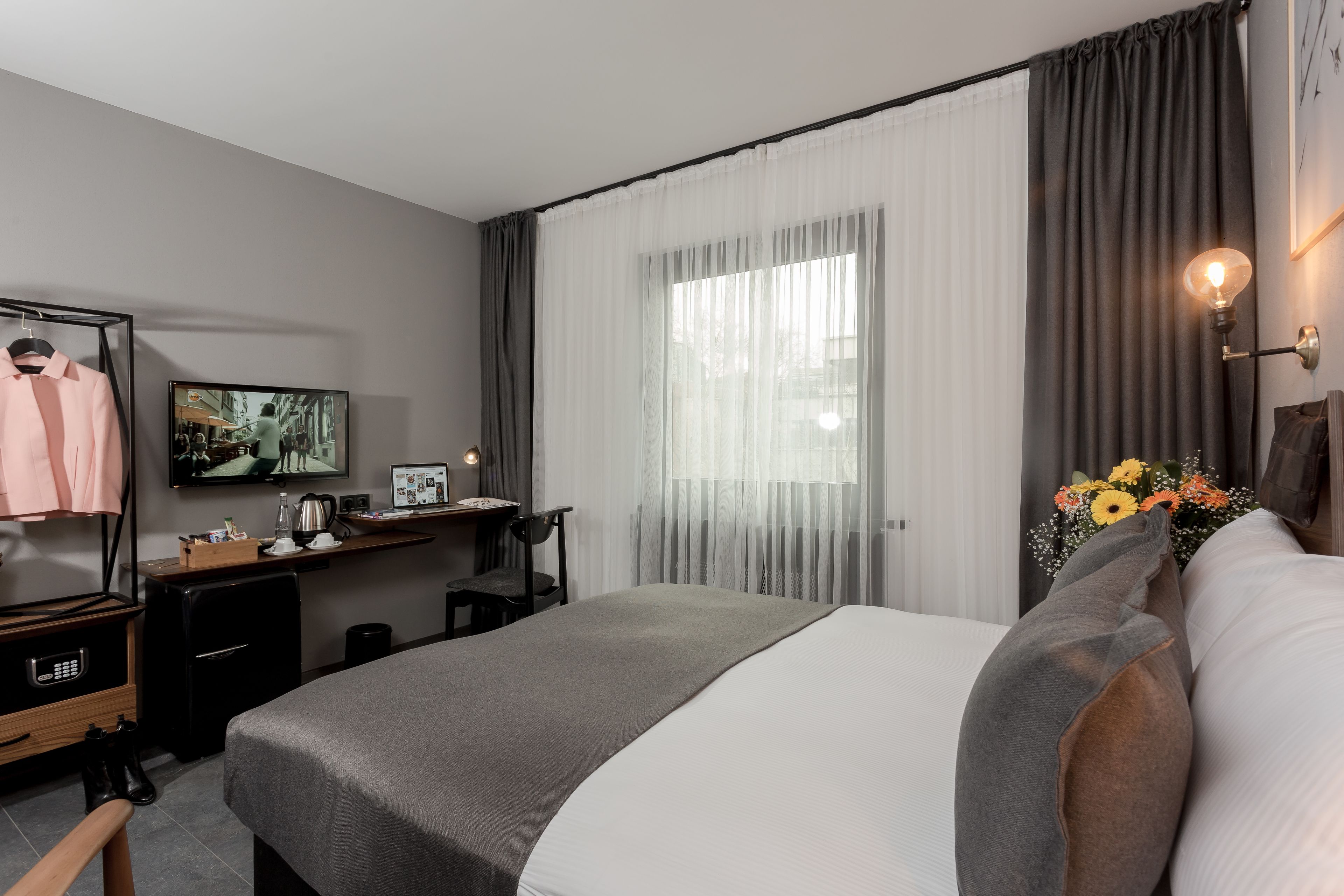 A modern hotel room with a bed, a desk, a TV, and a wardrobe.