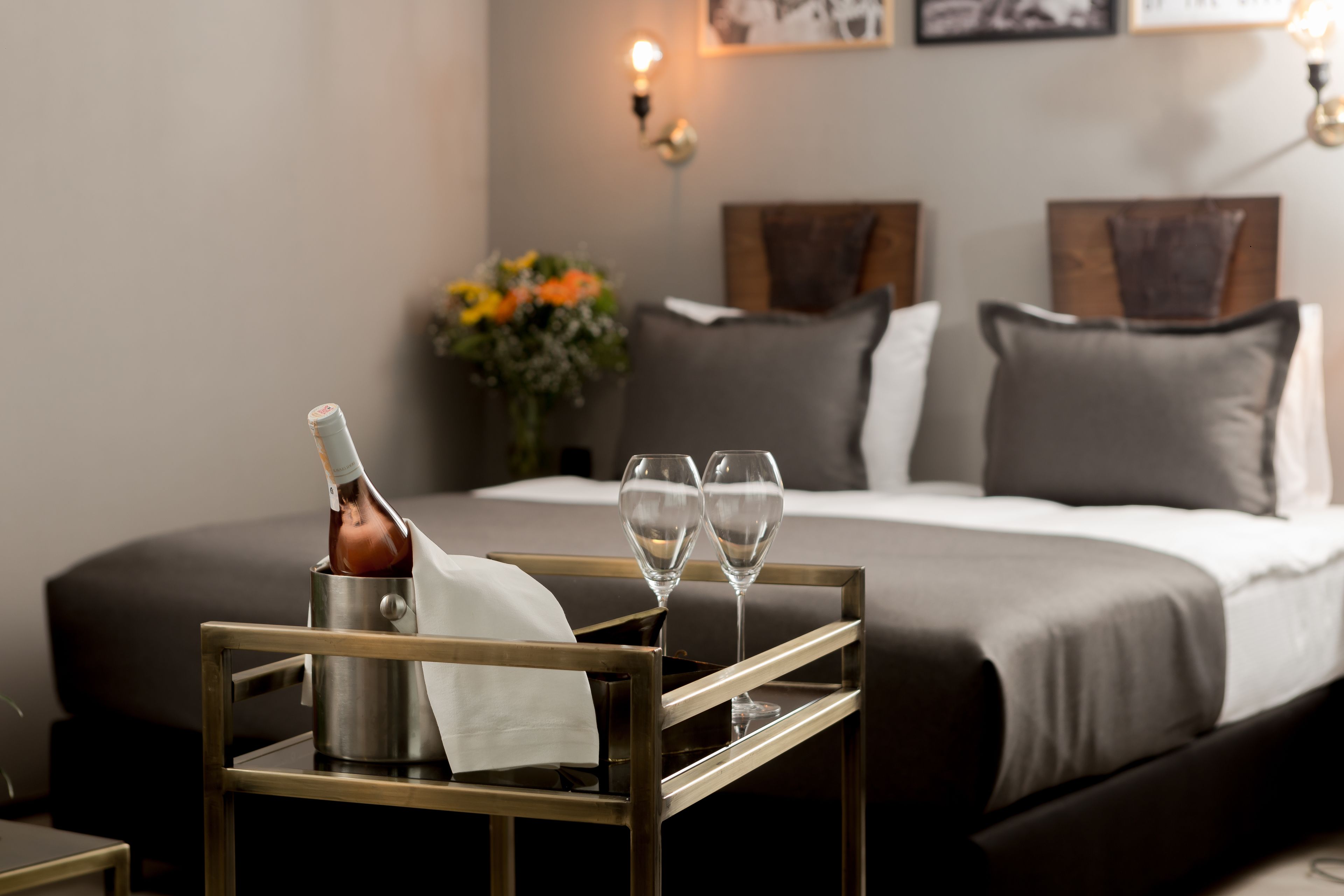 A bed with a black headboard, a bedside table with a bottle and glasses, and a wall-mounted light.