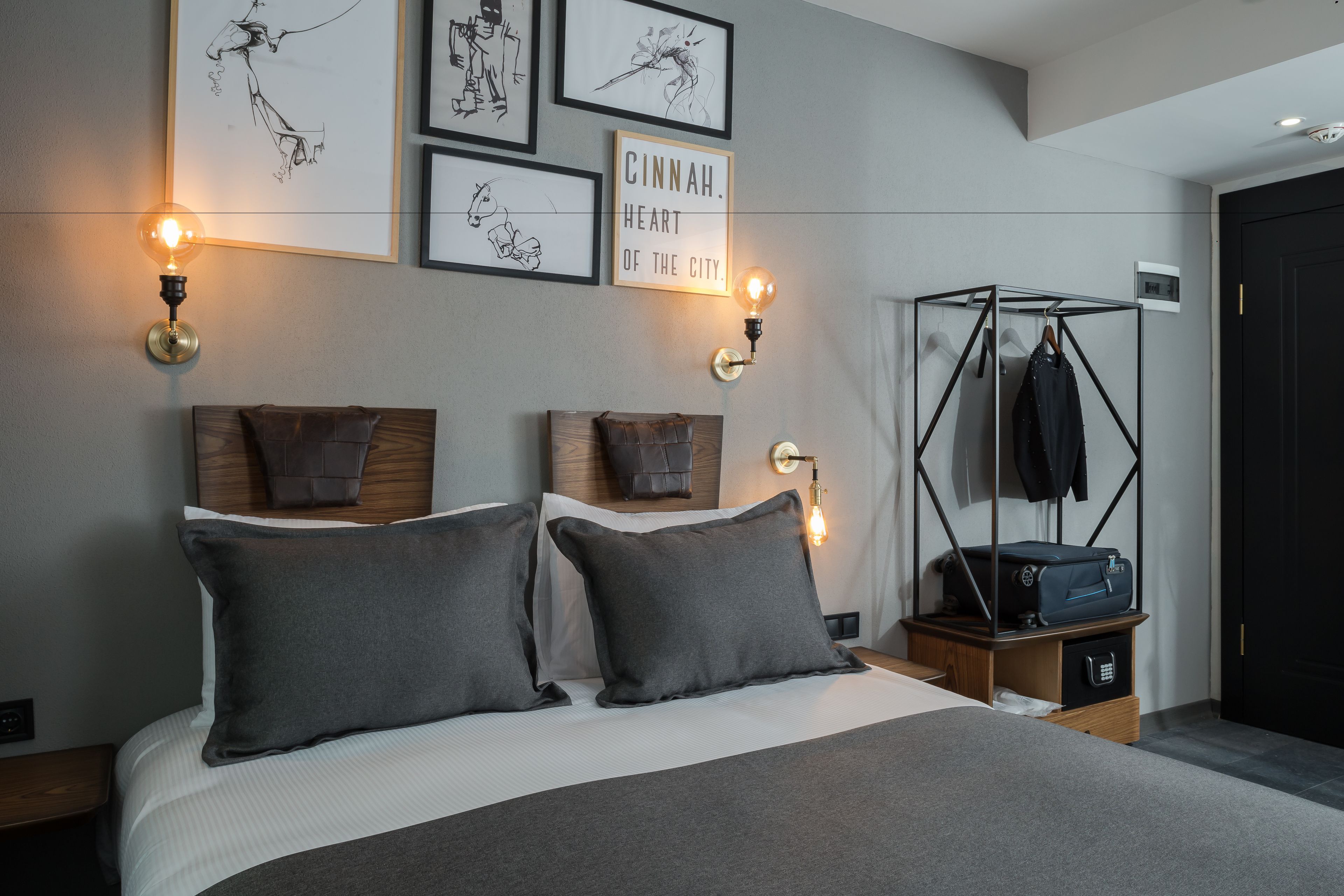 A modern hotel room with a bed, wall-mounted artwork, and a coat rack with luggage.