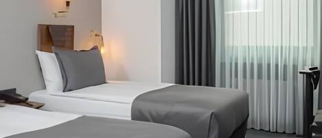 Una habitación de hotel con dos camas, una mesita de noche, una lámpara y un ventanal con cortinas.