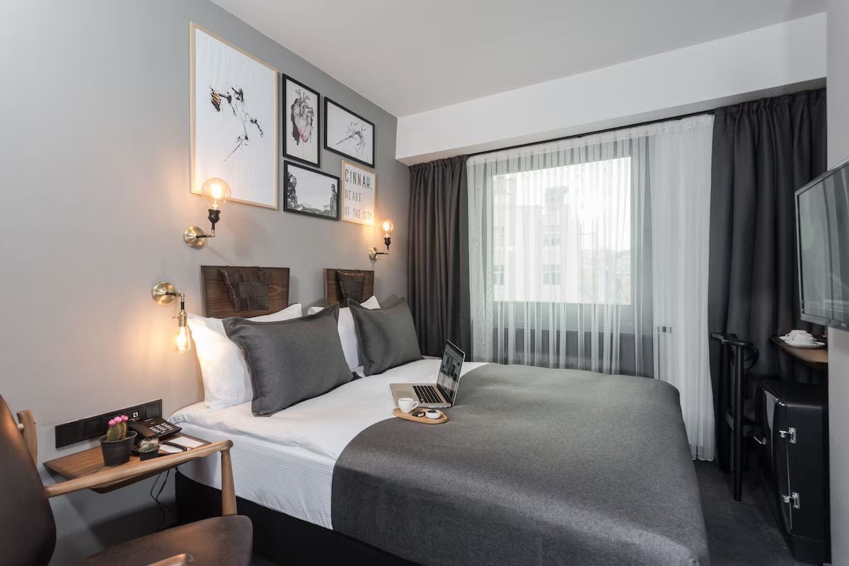 A hotel room with a large bed, a desk with a laptop, a chair, a TV, and artwork on the wall.