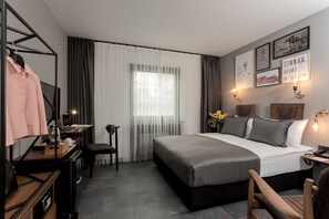 A modern hotel room with a bed, desk, chair, and a window with curtains.