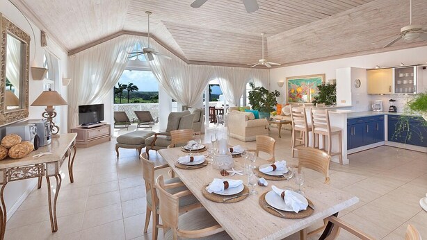 A spacious living area with a dining table set for four, a kitchen with blue cabinets, and a balcony with a view.