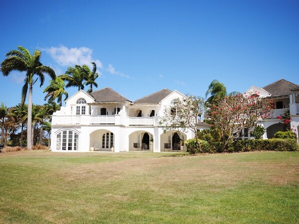A large, white, two-story house with a spacious front yard and palm trees.