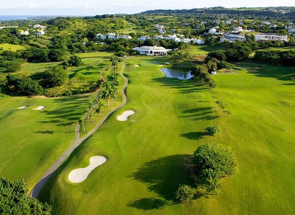 A golf course with sand bunkers, a pond, and residential houses in the background.