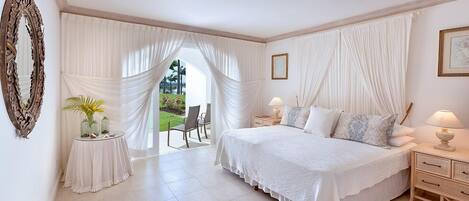 Un dormitorio con una cama grande, dos mesitas de noche con lámparas, un espejo y vistas a un jardín a través de cortinas translúcidas.