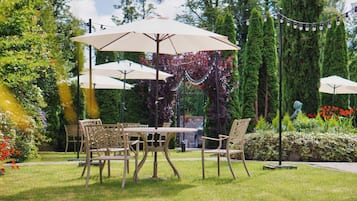 An outdoor seating area with tables and chairs under umbrellas, surrounded by greenery and decorative lights.