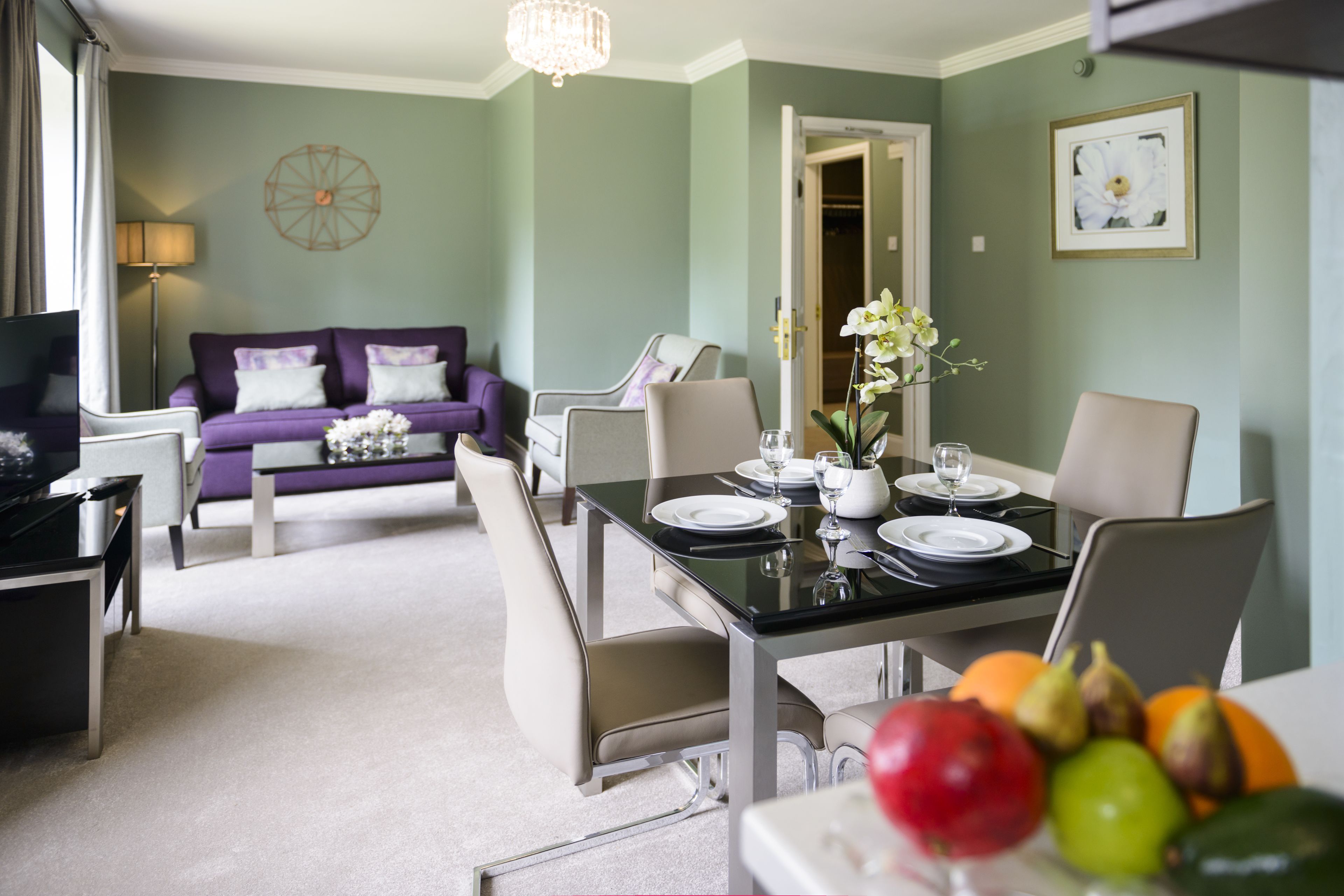 A dining area with a table set for two, a sofa, and a television in the background.