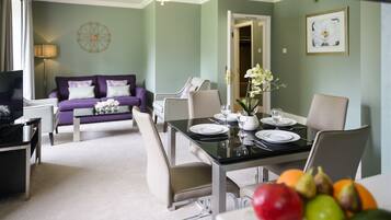 A dining area with a table set for two, a sofa, and a television in the background.