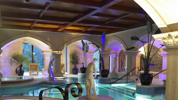 Un espace piscine intérieur luxueux, aménagé sur plusieurs niveaux et agrémenté d’une statue de femme.