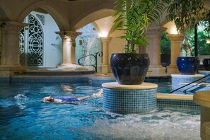 A swimming pool with a person swimming, surrounded by tiled walls and columns, with a large potted plant in the foreground. - The Reserve at Muckross (Killarney)